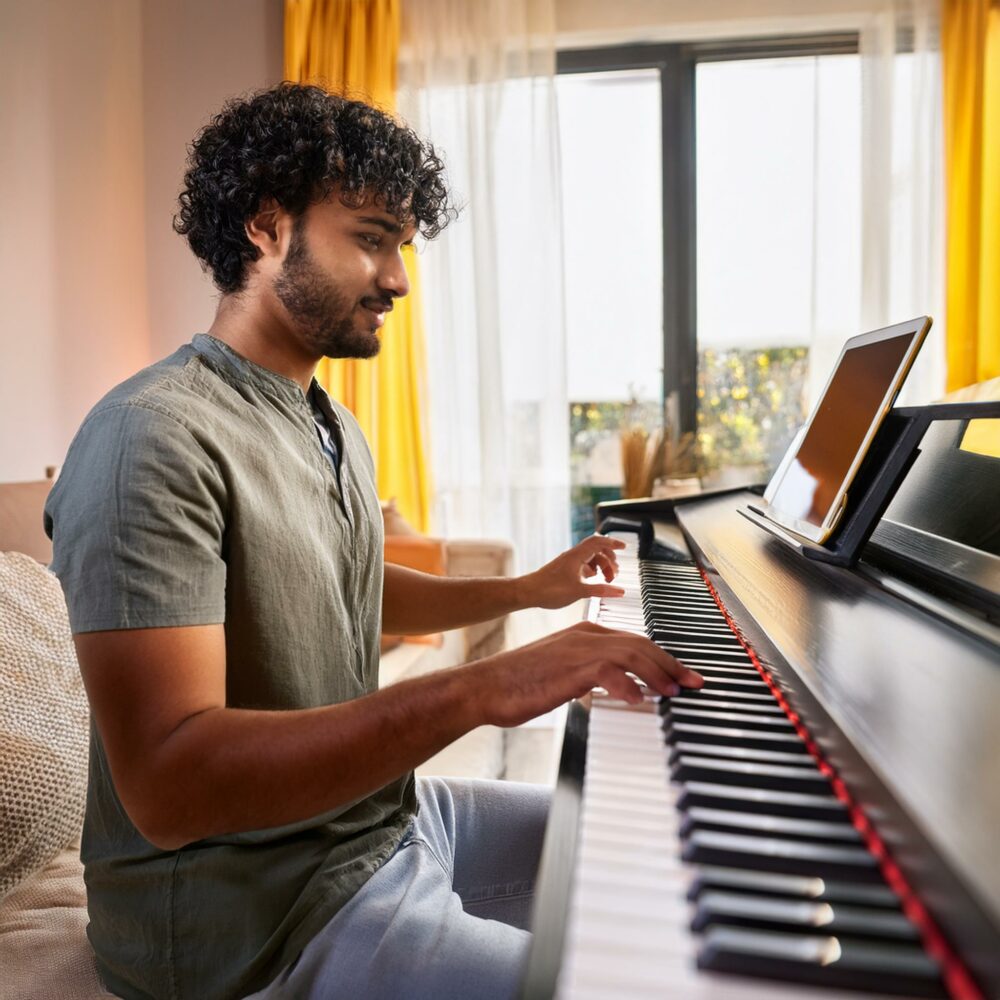 a young man learning piano after finding out How to Learn to Play Piano Online using a tablet computer for lessons